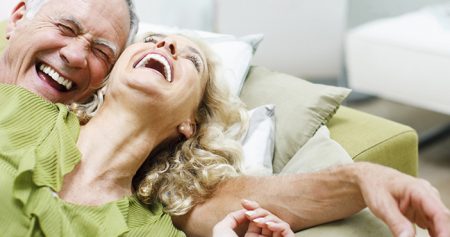 Älteres Paar liegt lachend auf der Couch.