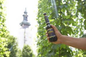 Eine Hand mit einer Bierflasche, dahinter in Kirchturm, Stichwort Wein und Bier. (c) Stift Schlägl/ Klösterreich