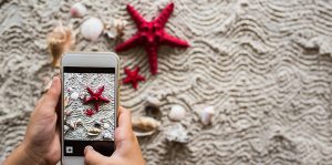 Jemand, der einen Seestern am Strand mit dem Smartphone fotografiert, Stichwort Kostenfallen. (c) Pixabay.com