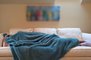 Ein Mann auf der Couch unter einer Decke, Stichwort 8 Stunden Schlaf täglich. (c) Pixabay.com