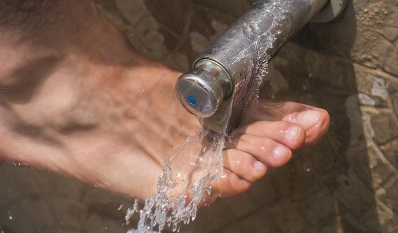 Ein Mann, der seinen Fuß unter fließendes Wasser hält. (c) Pixabay.com