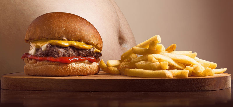 Ein Burger und Pommes, dahinter ein Mann mit dickem nackten Bauch.  (c) Pixabay.com