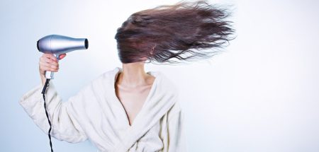 Eine Frau im Bademantel, die mit einem Föhn ihre langen Haare zur Seite bläst. (c) Pixabay.com