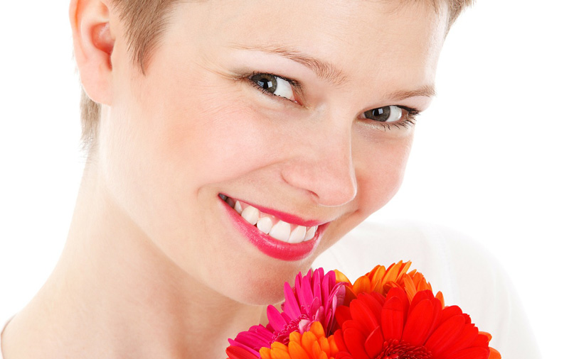 Der Kopf einer lächelnden Frau, die Blumen zu ihrem Gesicht hält, Stichwort froh zu sein. 
(c) Pixabay.com