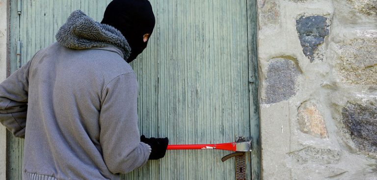 Ein Einbrecher mit Gesichtsmaske, der mit einem Brecheisen eine Tür aufbricht. (c) Pixabay.com