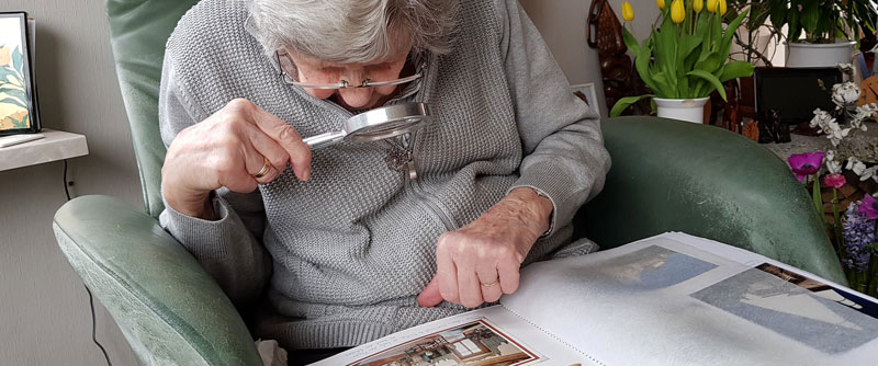 Eine alte Frau, die sich mit Hilfe einer Lupe ein Fotoalbum anschaut. (c) Pixabay.com