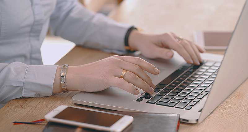 Hände auf einer Laptoptastatur, daneben ein Smartphone auf einem Notizbuch – praktisch, wenn man seine Amtswege online erledigen kann. (c) Pixabay.com