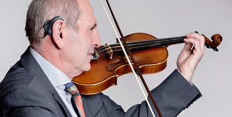 Ein älterer Mann mit einem Hörimplantat spielt Geige – gerade beim Musizieren ist gut Hören sehr wichtig. (c) MED-EL