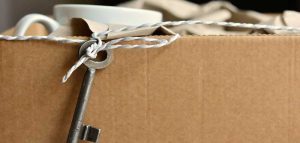 Frauen ziehen wegen der Liebe um, Männer wegen der Wohnung Ein Schlüssel, der an einer Schnur über einen Karton hängt, auf dem Klebeband liegt. (c) Pixabay.com