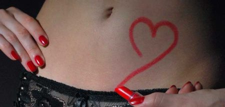 Eine Frau, die mit rotem Lippenstift ein Herz auf ihren Bauch zeichnet. (c) Pixabay.com