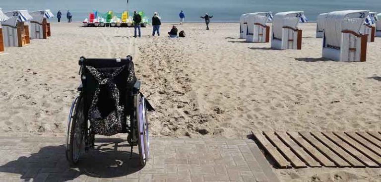 Barrierefrei reisen ist oft gar nicht so einfach. Ein leerer Rollstuhl vor einem Sandstrand. (c) Pixabay.com