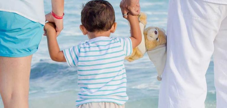 Ein kleines Kind in der Mitte Hand in Hand mit seinen Eltern, im Hintergrund das Meer. (c) Pixabay.com