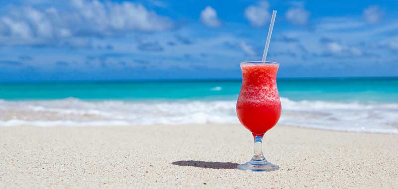 Ein Cocktailglas auf einem Sandstrand, dahinter das Meer. (c) Pixabay.com