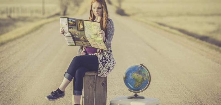 Eine Frau mit einer Karte in der Hand sitzt mitten auf der Straße auf einem Koffer, neben ihr steht ein kleiner Globus. (c) Pixabay.com