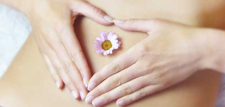 Der Bauch einer Frau mit einer Blüte im Bachnabel und ihren Händen darum, die ein Herz bilden. (c) Pixabay.com