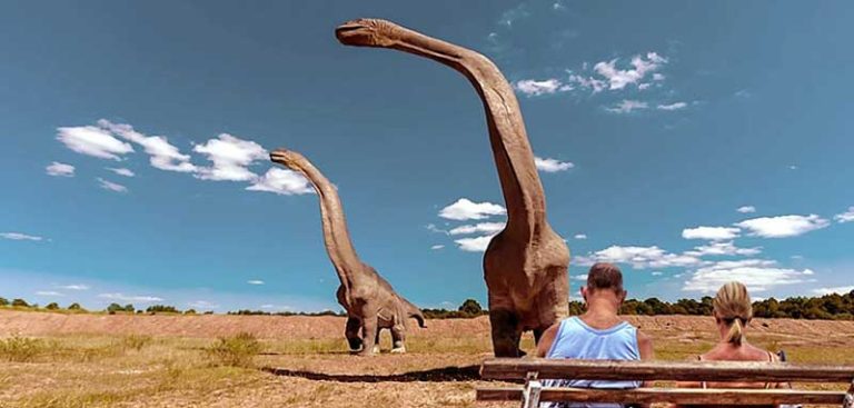 Ein Paar auf einer Bank vor zwei riesigen Dinosauriern. (c) Pixabay.com