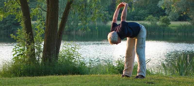 #BewegungISTgesund – für Gesundheit und Wohlbefinden im Alter 1 Bewegung ist gesund – ein älterer Mann beim Dehnen seines Rückens an einem See. (c) Pixabay.com