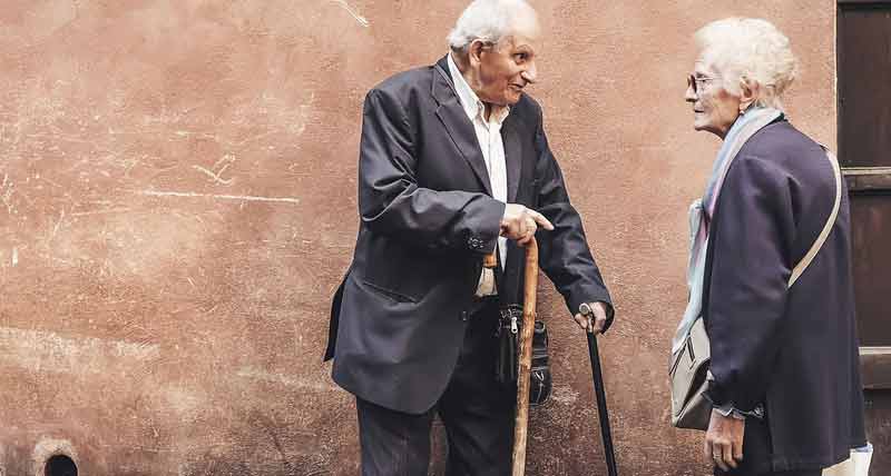 Ein alter Mann und eine alte Frau vor einem Haus im Gespräch miteinander. (c) Pixabay.com