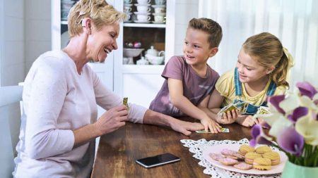 Eine Frau mit einem Cochlea-Implantat mit zwei Kindern an einem Tisch beim Karten Spielen. (c) Cochlear Ltd.