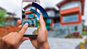 Das smarte zu Hause – wenn die moderne Technik daheim einzieht Jemand, der vor einem smarten Haus stehend mit seinem Handy diverse Einstellungen steuert. (c) Pixabay.com