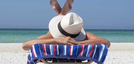 Eine Frau mit Sonnenhut liegt auf dem Bauch auf einer Liege auf einem Strand und lässt sich sonnen. (c) Pixabay.com