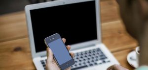 Digitaler Einfluss – Wie Bildschirme der Augengesundheit schaden Hand eines Mannes, der vor einem Laptopbildschirm ein Smartphone hält. (c) Pixabay.com