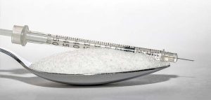 Ein Teelöffel voll Zucker vor einer Insulinspritze. (c) Pixabay.com