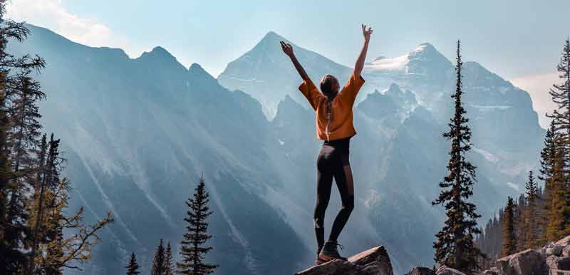 Eine Frau auf einem Felsen streckt die Hände in die Luft. (c) Pixabay.com