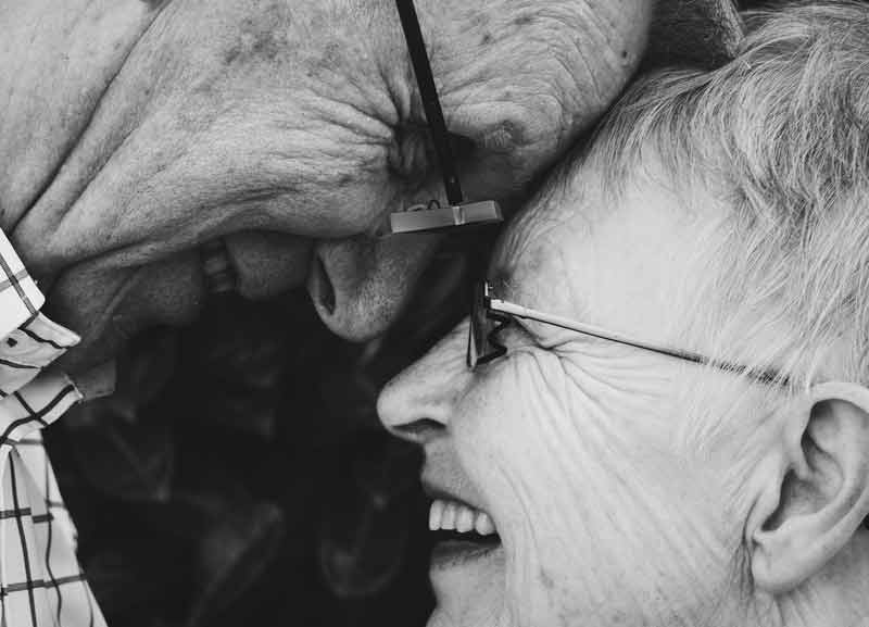 Ein altes Paar, das sich mit der Stirn gegenseitig berührt uns anlacht. (c) Pixabay.com