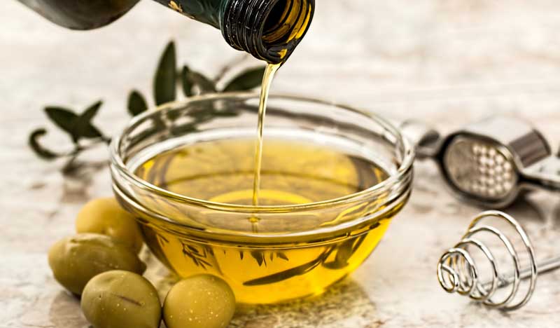 Olivenöl wird in eine kleine Schüssel geleert, vor der grüne Oliven liegen. (c) Pixabay.com