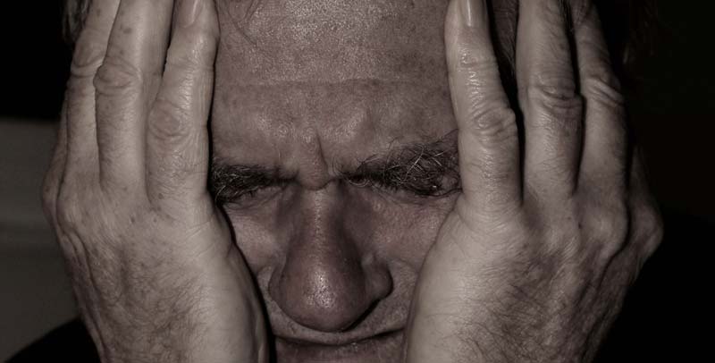 Das Gesicht eines alten Mannes, der sich vor Schmerz mit beiden Händen den Kopf hält, Stichwort Tinnitus. (c) Pixabay.com