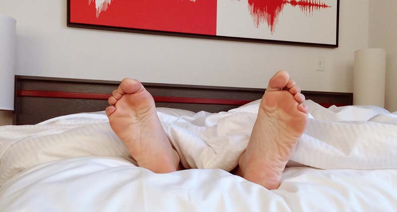 Die Füße einer im Bett liegenden Person, die unter der Decke hervor schauen. (c) Pixabay.com