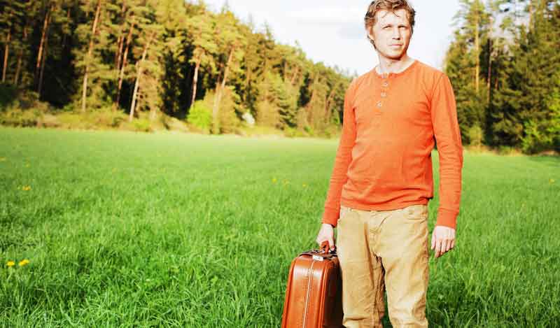 Ein Mann mit einem Koffer in der Hand auf einer Wiese, Stichwort Alleinreisende. (c) Pixabay.com