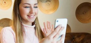 Ein lächelndes Mädchen, das in ihr Handy winkt. (c) Pixabay.com