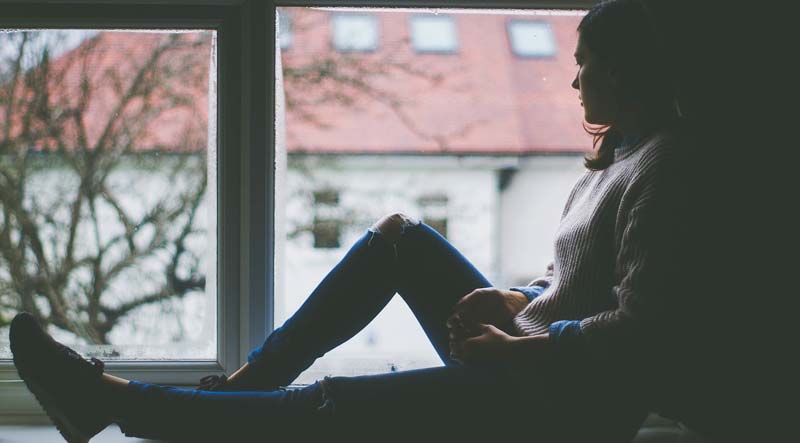Eine Frau, die traurig am Fensterbrett sitzend beim Fenster rausschaut, Stichwort depressive Verstimmung.
(c) Pixabay.com