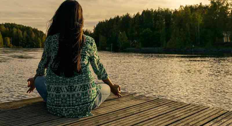 Eine Frau, die an einem See auf einem Steg in einer Yoga-Position sitzt.
(c) Pixabay.com
