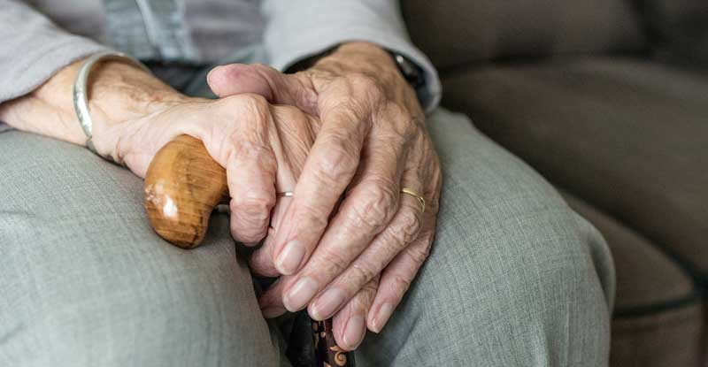 Die Hände einer sitzenden alten Frau auf dem Griff eines Gehstocks.
(c) Pixabay.com