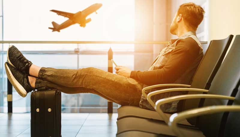 Corona-Regeln in beliebten Urlaubsländern: Darauf sollten sie achten 1 Ein Mann mit seinen Beinen auf seinem Reisekoffer schaut durch das Fenster einem startenden Flugzeug zu, Stichwort Corona-Regeln.
(c) Pixabay.com