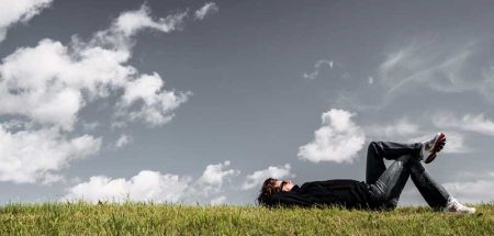 Eine Frau, die auf dem Rücken auf einer Wiese liegt und in den Himmel schaut. (c) Pixabay.com