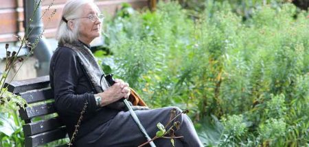 Eine alte Frau sitzt neben einer Wiese auf einer Bank. (c) Pixabay.com