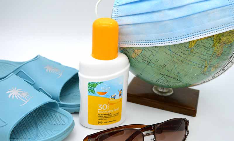 Ein Globus mit einer Mund-Nasen-Schutzmaske, daneben eine Sonnenbrille, Sonnencreme und Badeschlapfen.
(c) Pixabay.com