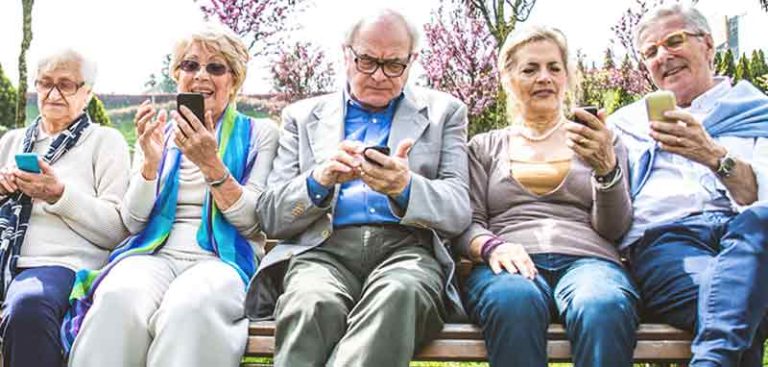 5 Senioren auf einer Bank im Freien, die alle mit ihrem Smartphone beschäftigt sind. (c) Doro