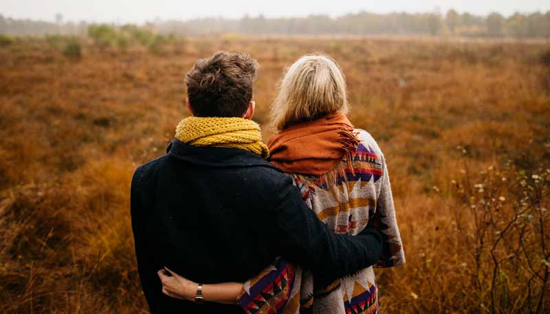 Ein Mann und eine Frau umschlungen vor einer herbstlich gefärbten Wiese.
(c) Pixabay.com