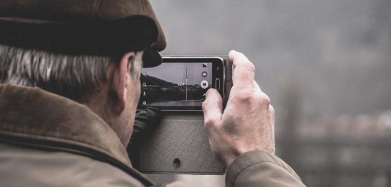 Der Kopf eines älteren Mannes von hinten, der gerade mit seinem Smartphone ein Foto macht. (c) Pixabay.com
