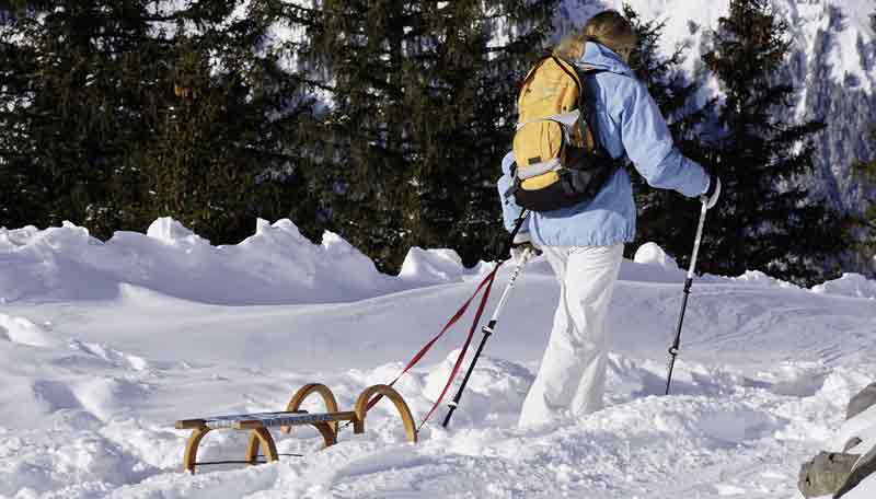 Eine Frau beim Wandern im Schnee mit einer Rodel, die sie hinter sich herzieht.
(c) Pixabay.com