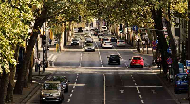 Eine befahrene Straße in einer Stadt, an deren Rändern links und rechts Bäume stehen, Stichwort automatisierte Fahrtechnologie.
(c) Pixabay.com