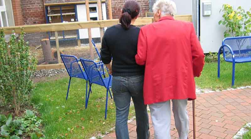 Eine Pflegerin, die mit einer alten Frau, die ihren Arm bei ihr eingehängt hat, spazieren geht.
(c) Pixabay.com