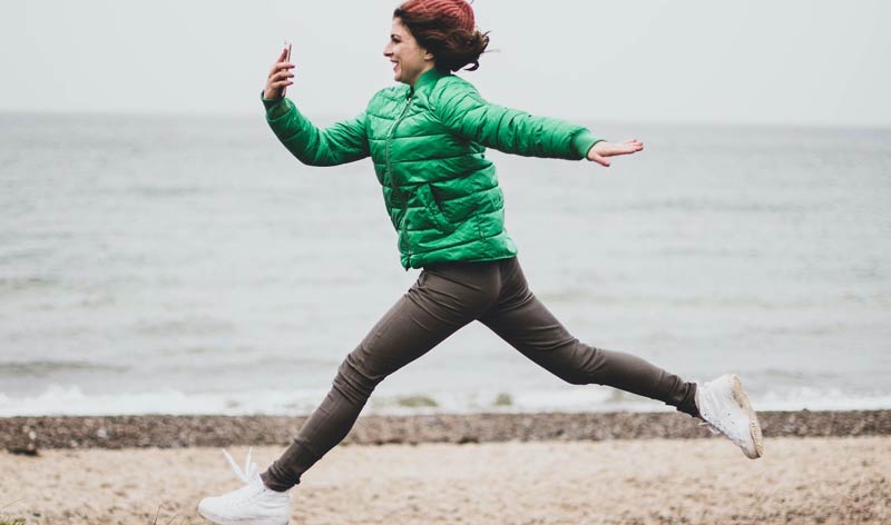 Eine Frau, die auf einem Strand springt und dabei freudig auf ihr Smartphone schaut, Stichwort Gesundheitsapp.
(c) trueplus