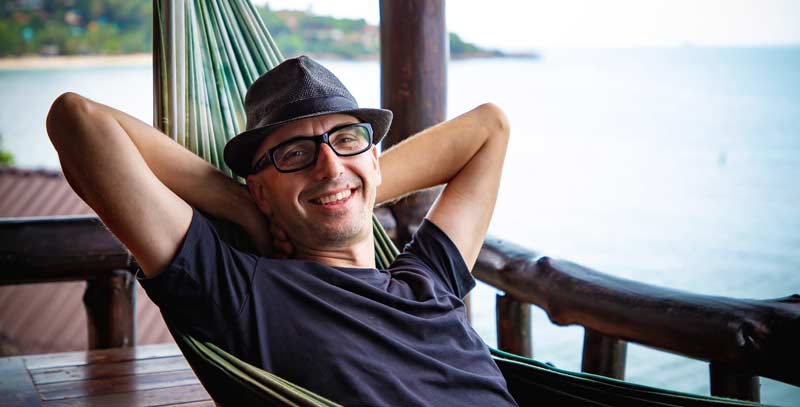 Ein Mann mit Hut und Brille in einer Hängematte, dahinter ein See.
(c) Pixabay.com