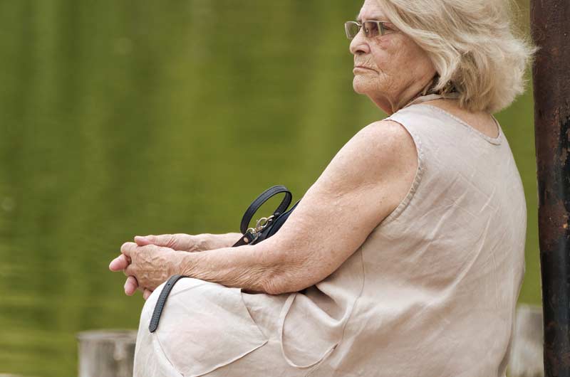 Eine ältere Frau sitzt an einem See und schaut in die Ferne, Stichwort Betätigungsbalance.
(c) Pixabay.com